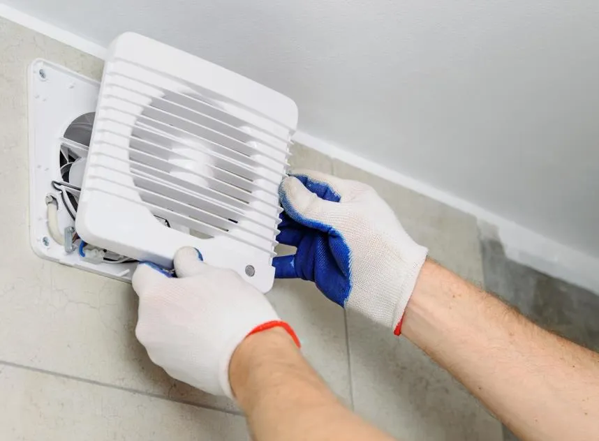 Gloved hands fitting an exhaust fan to a wall