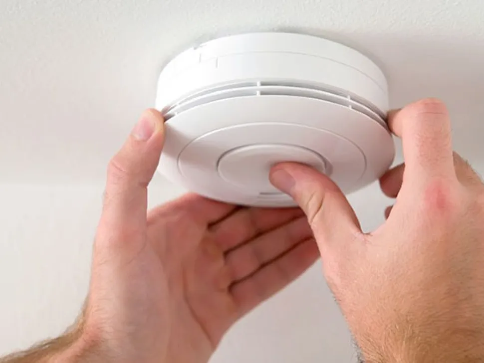 Hands fitting a smoke alarm to a ceiling