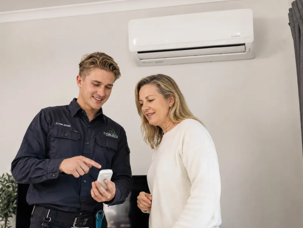 Electrician showing a woman a remote under a split system air conditioner