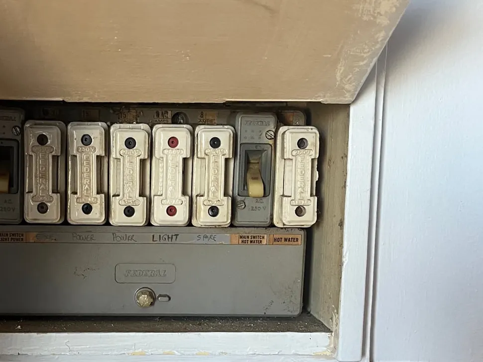 Old switchboard with rewireable fuse carriers and a dated meter board, before replacement