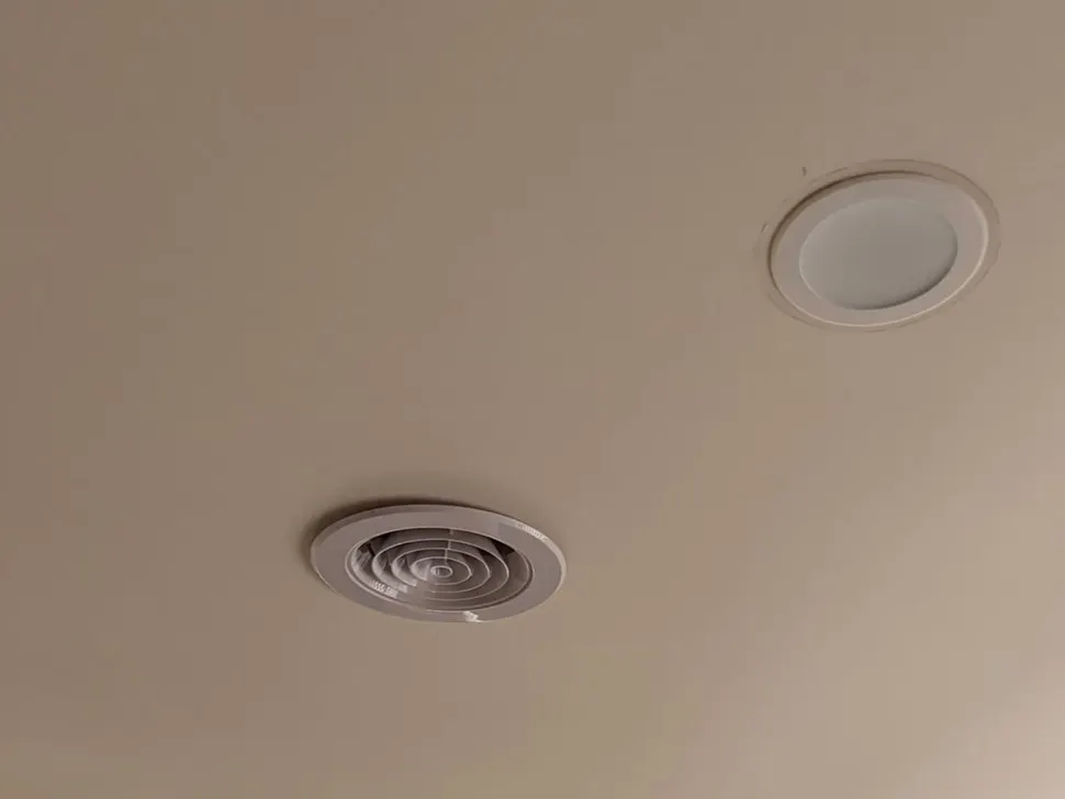 Flat white recessed downlight in a plain ceiling beside a round vent