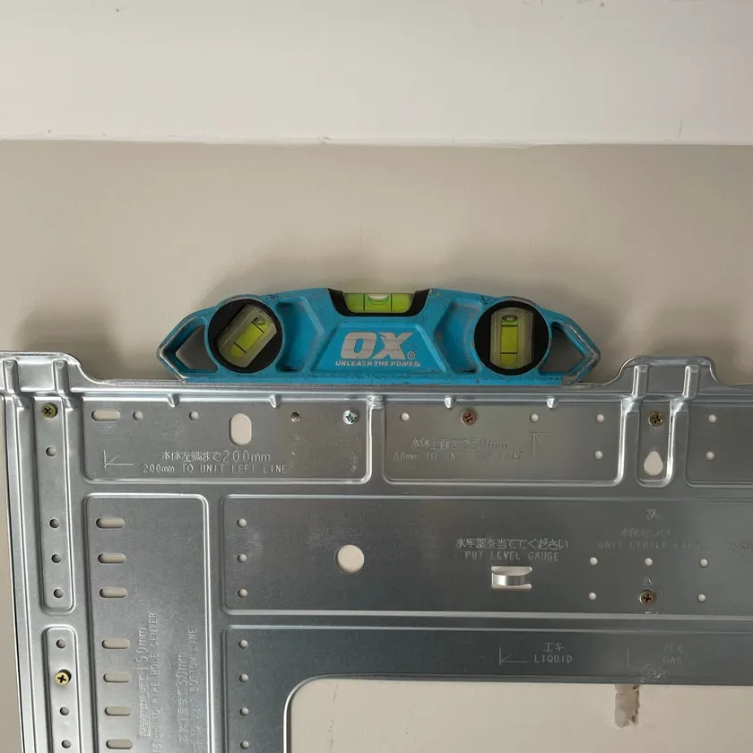 Split system indoor unit mounting plate fixed to a wall with a spirit level sitting on top of it