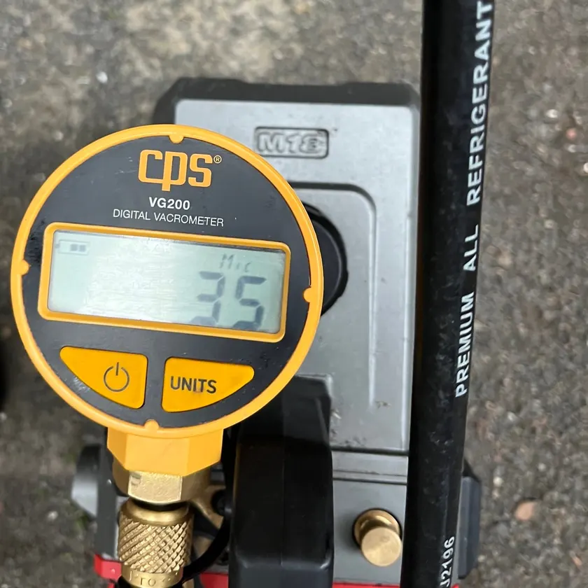 Digital vacuum gauge connected to a refrigerant charging hose and vacuum pump during an air conditioner installation