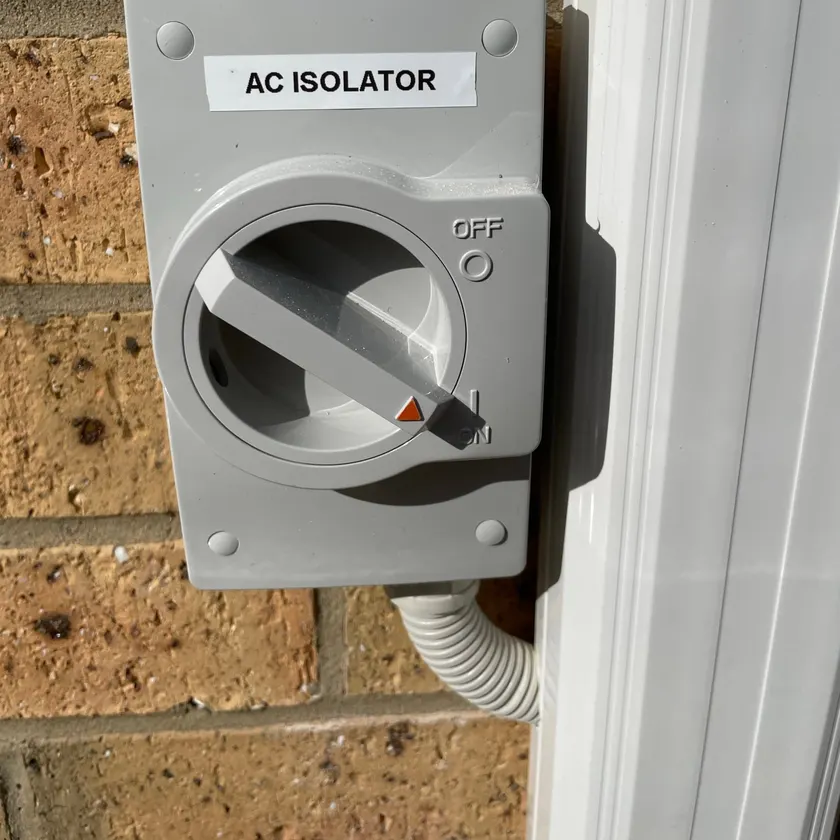 Weatherproof outdoor isolator switch labelled AC ISOLATOR mounted on a brick wall