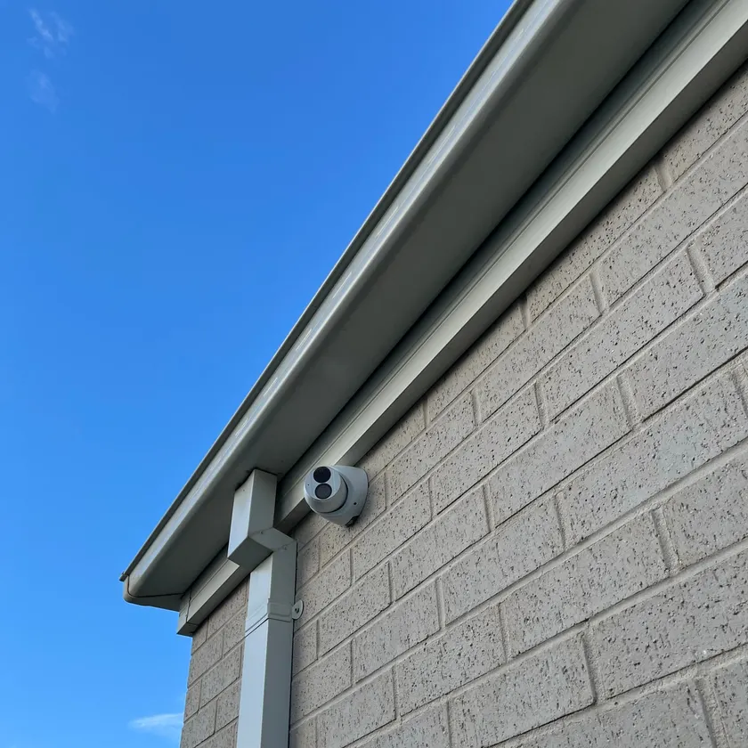 White turret security camera fixed to a brick wall beneath the gutter line