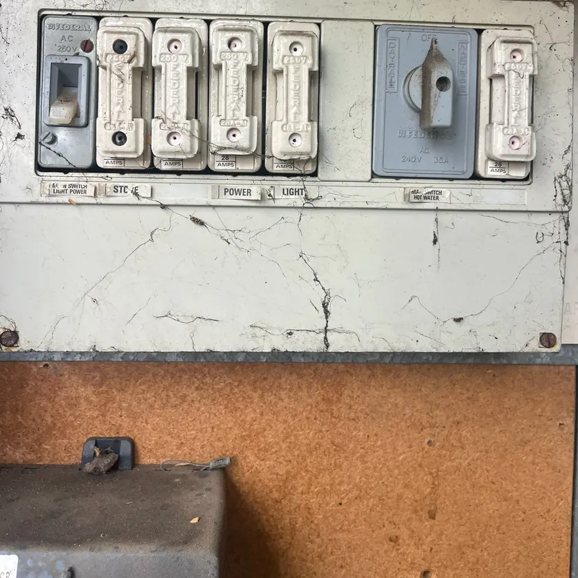 Old switchboard with ceramic rewirable fuses and an old main switch, covered in cobwebs