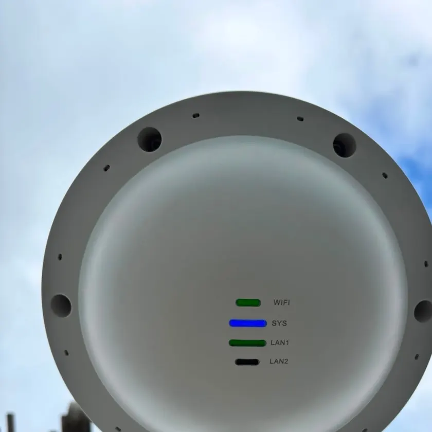 Round white outdoor wireless access point on a pole mount with status lights on