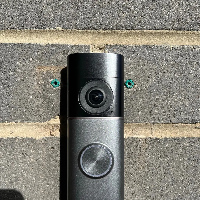 Black video doorbell mounted on a dark brick wall