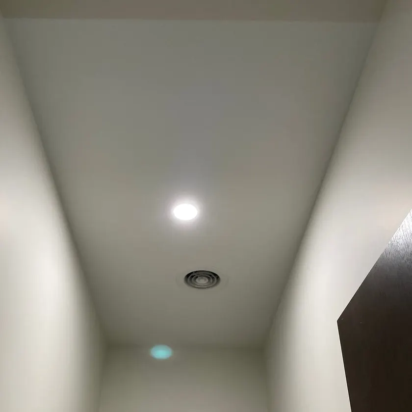 Round recessed downlight beside an exhaust fan grille on a white ceiling
