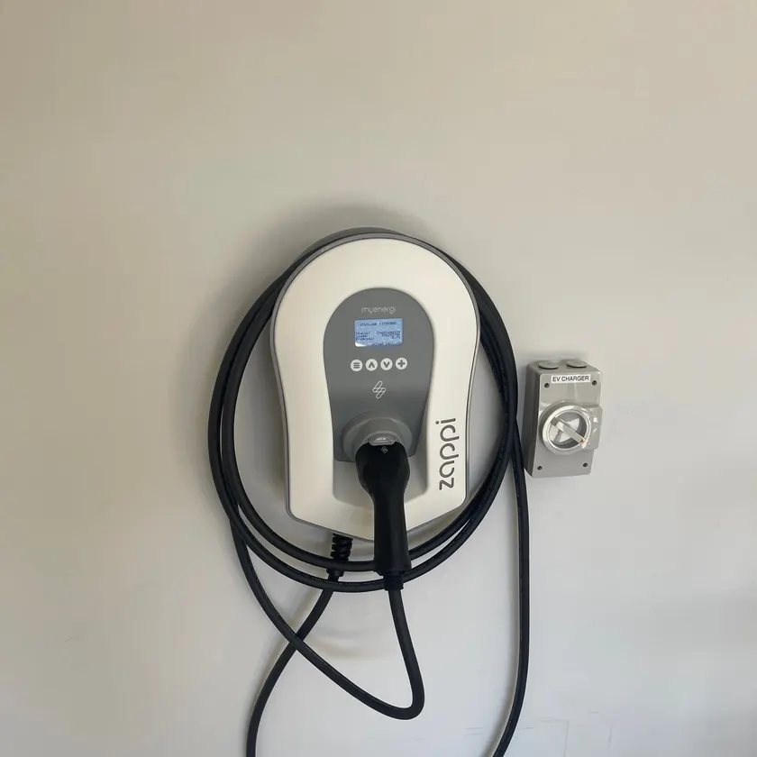 White wall-mounted EV charger with coiled cable beside a labelled isolator switch