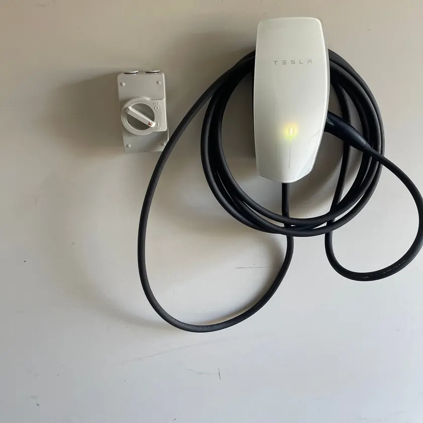 White wall connector EV charger with its cable wrapped, next to an isolator switch