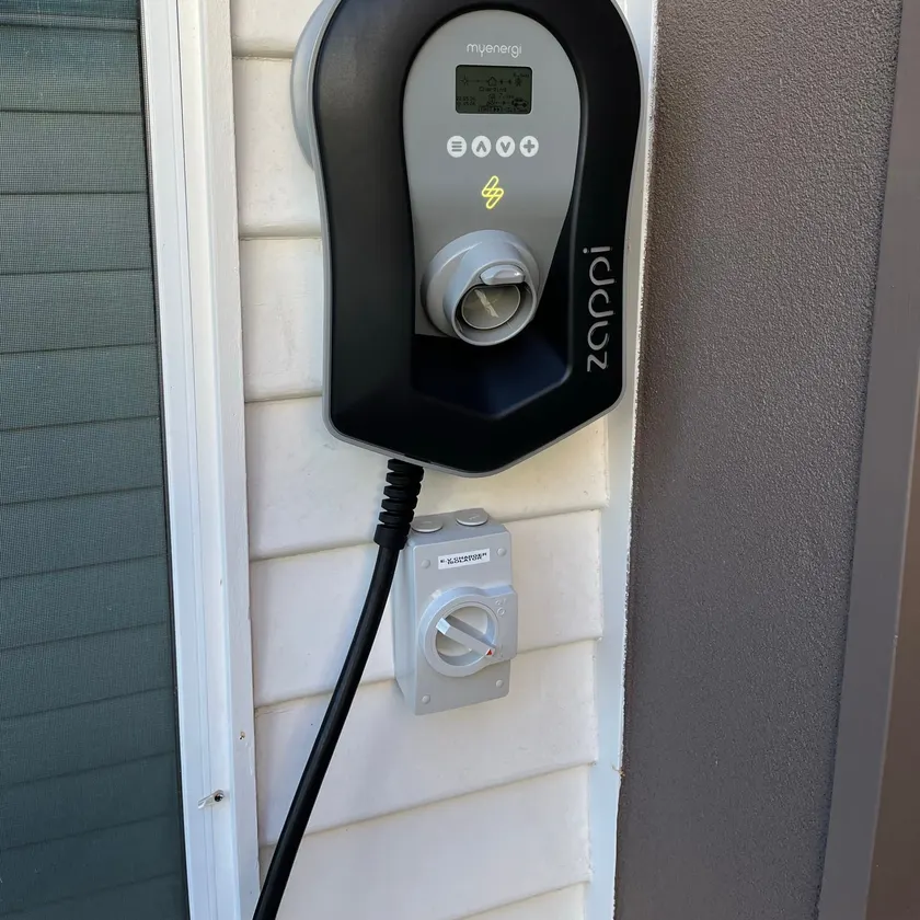 Black EV charger on a weatherboard wall with a labelled EV charger isolator