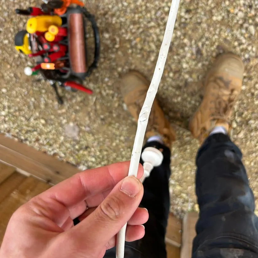 Damaged lead beside a hand, boots and a tool basket on a brick path
