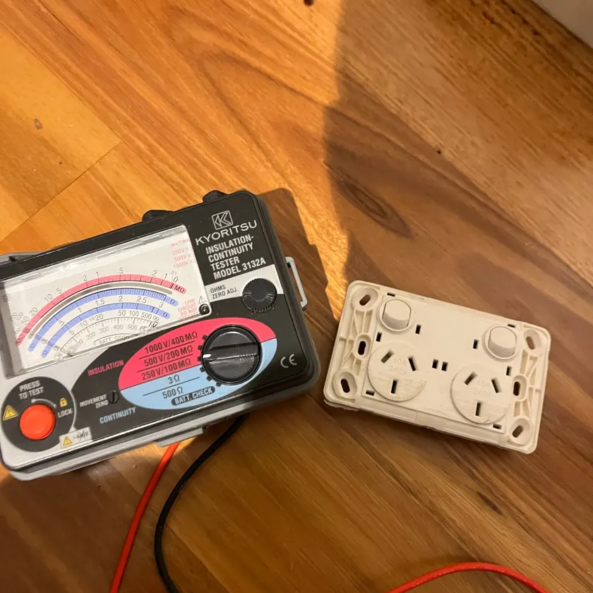 insulation tester beside a removed double power point on a timber floor