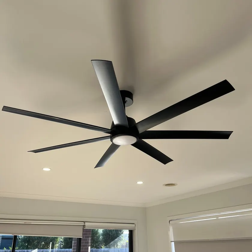 Black seven-blade ceiling fan with built-in light, fitted to a living room ceiling beside recessed downlights
