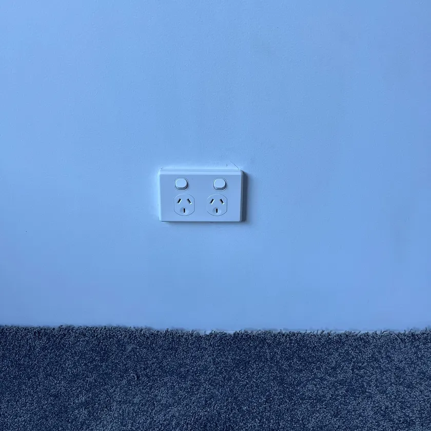 White double power point with switches mounted square on a plain painted wall above carpet