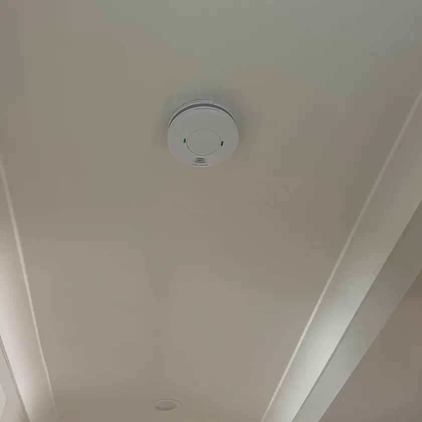 White interconnected smoke alarm with a green indicator light fitted to a ceiling between plaster cornices