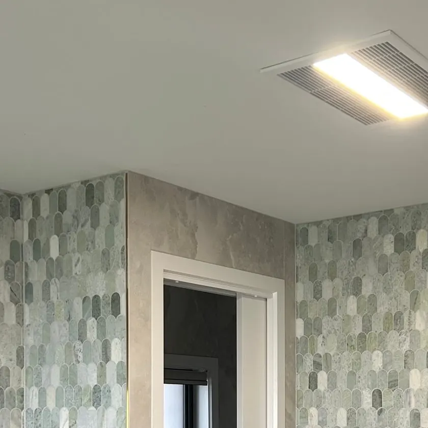 Ceiling mounted exhaust fan with built-in LED light above a tiled bathroom with a pocket door