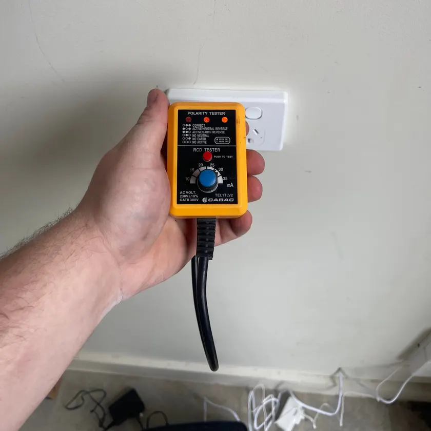 Hand and forearm holding a polarity and RCD tester plugged into a power point