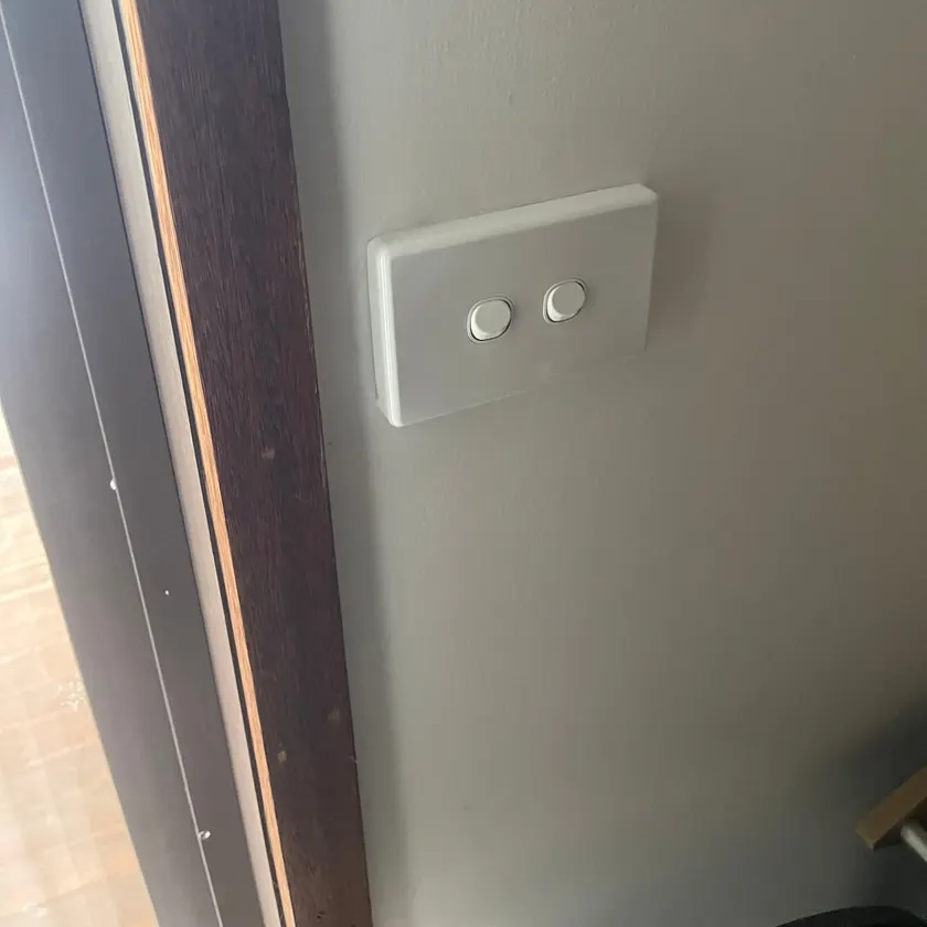 Plain two-gang light switch plate fitted beside a timber door frame