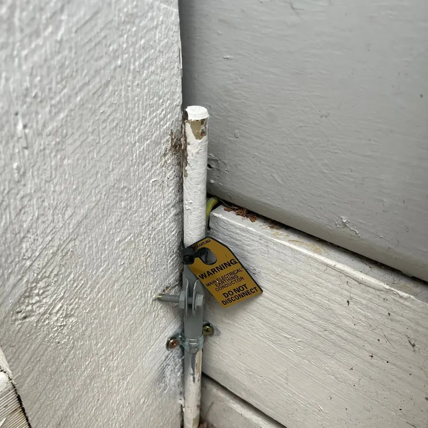 Earth electrode with a Do Not Disconnect tag at a wall base