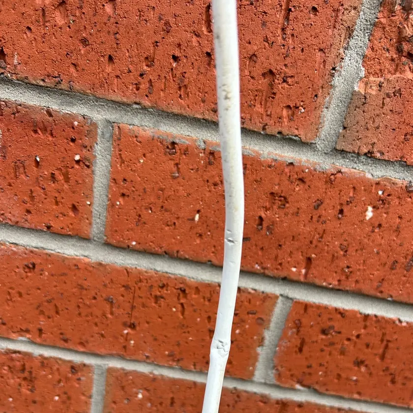 Damaged white power lead running along a brick wall with a split in the insulation