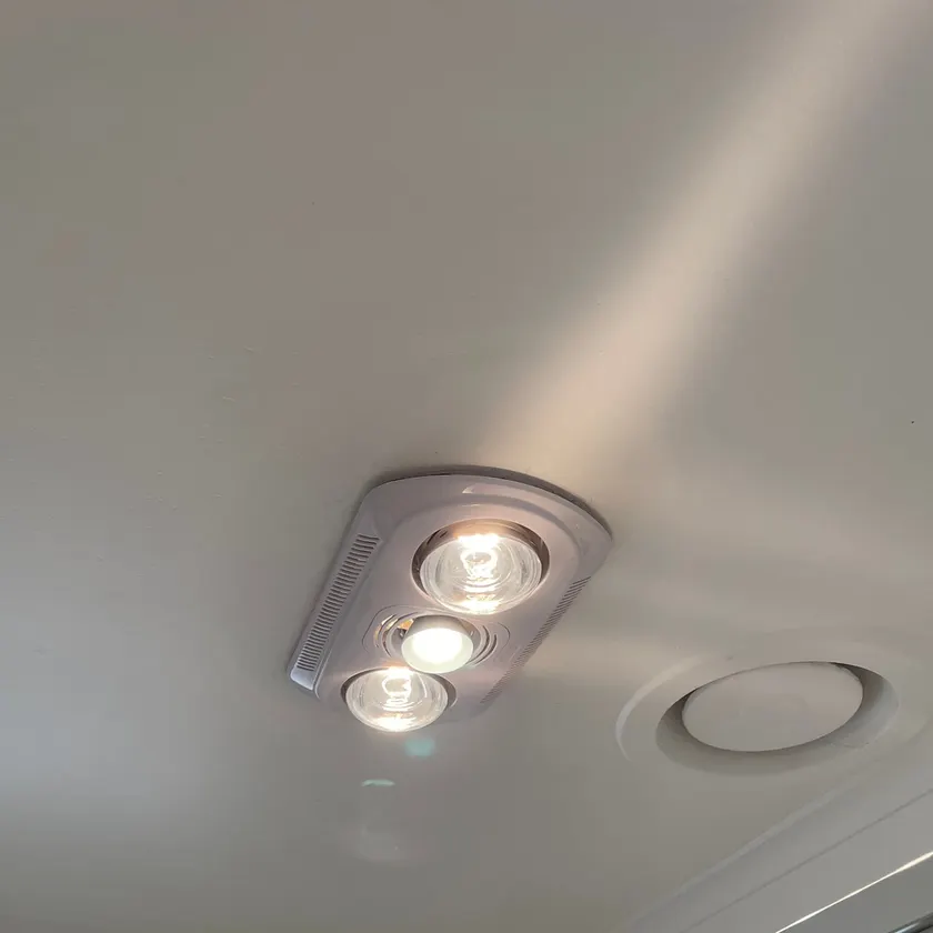 Bathroom ceiling unit with two heat lamps and a centre light, switched on