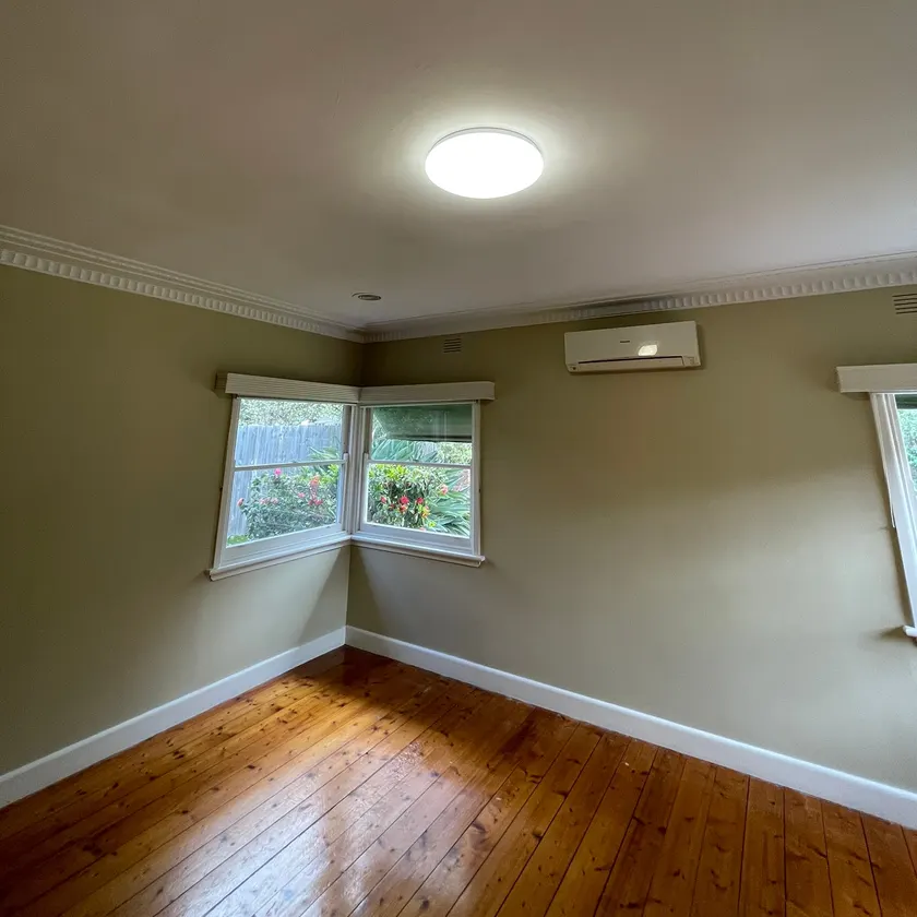 New round white LED ceiling light glowing in an empty bedroom with timber floor and corner windows