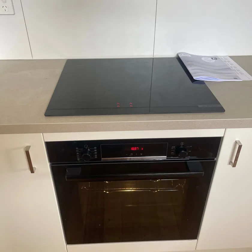 Black wall oven under a ceramic cooktop in a white kitchen