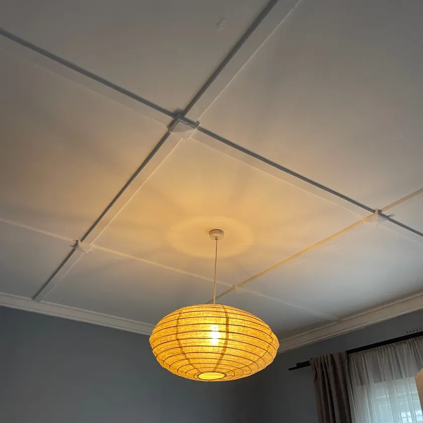 Paper lantern pendant light, lit, hanging from a panelled ceiling