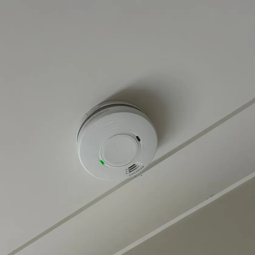 White smoke alarm on a ceiling with a green power light