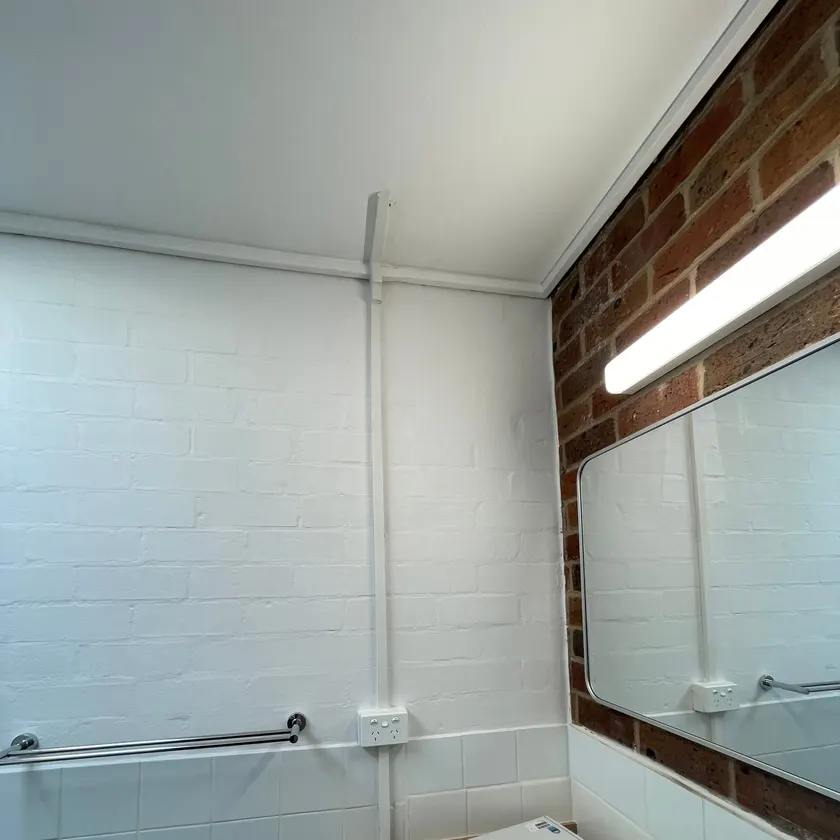 White double power point on a painted brick bathroom wall with neat white conduit run from the ceiling