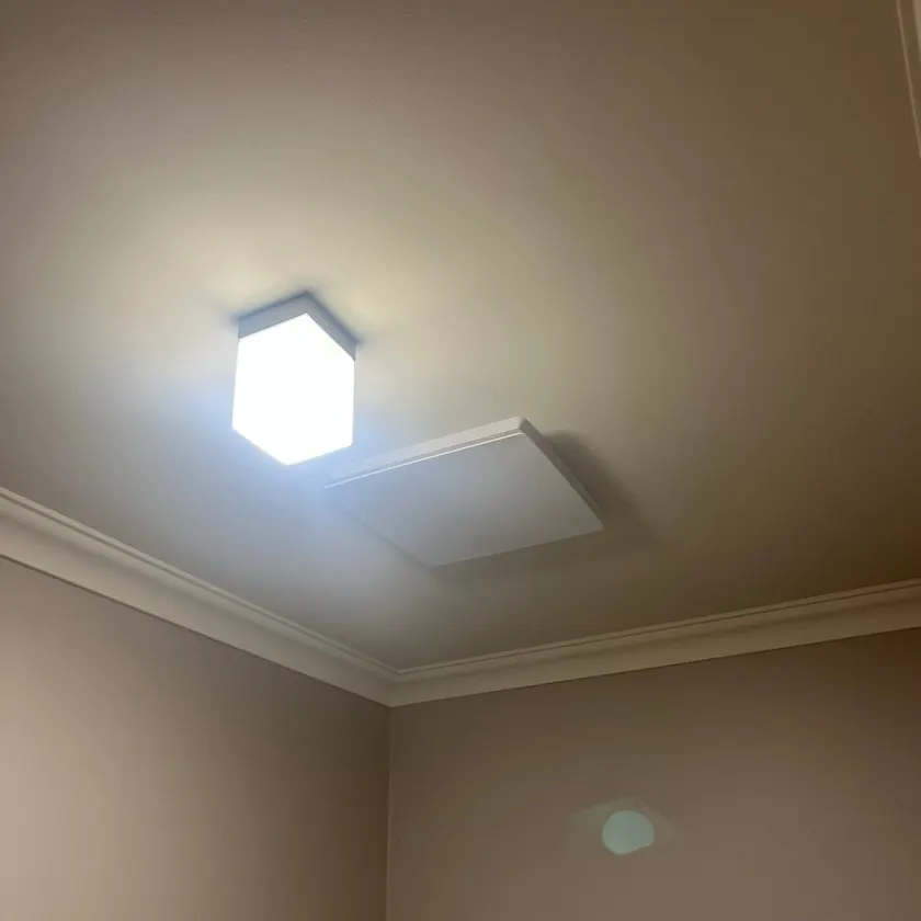 Square LED ceiling light and white exhaust fan cover installed side by side on a bathroom ceiling