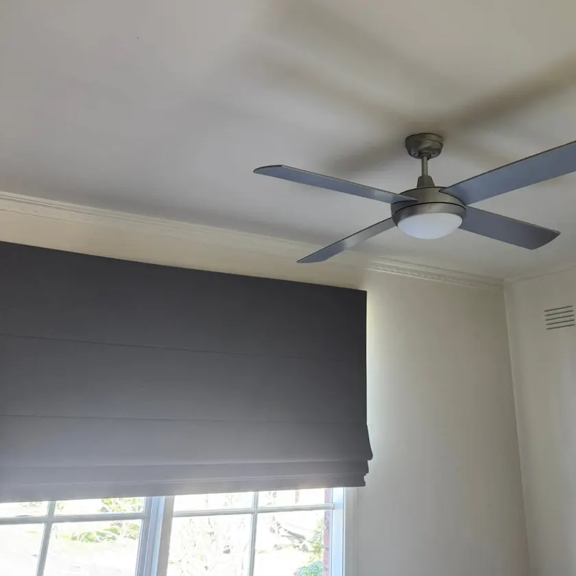 Four-blade ceiling fan with light fitted on a plain ceiling beside a window blind