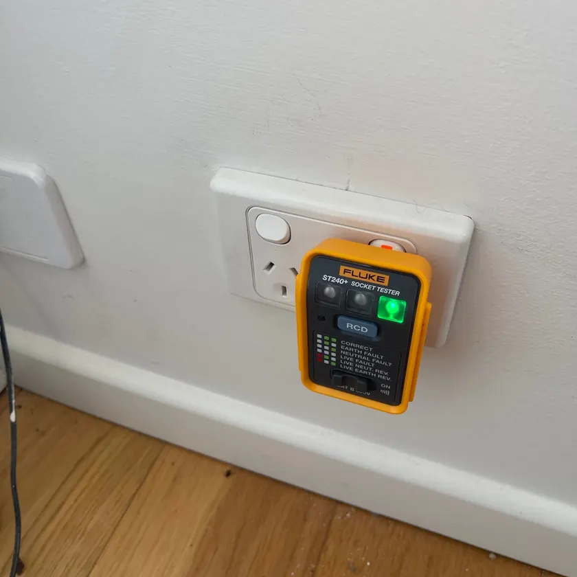 White double power point on a painted wall with a socket tester plugged in showing a green correct-wiring light