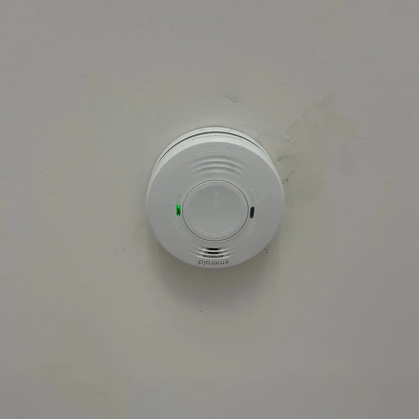 White smoke alarm fitted to a white ceiling