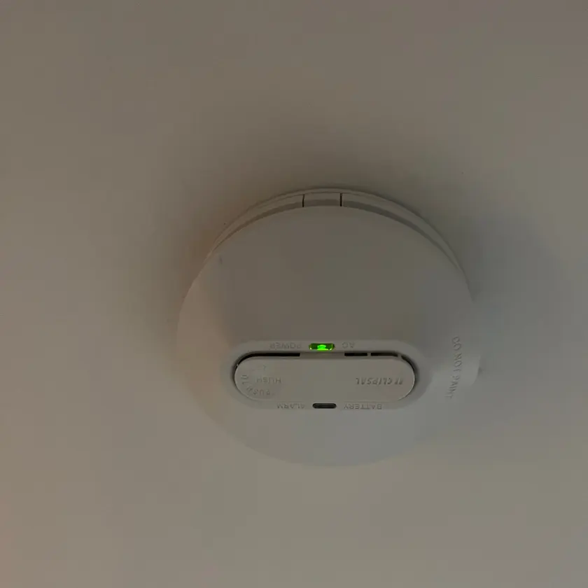 White smoke alarm on a ceiling with a green power light