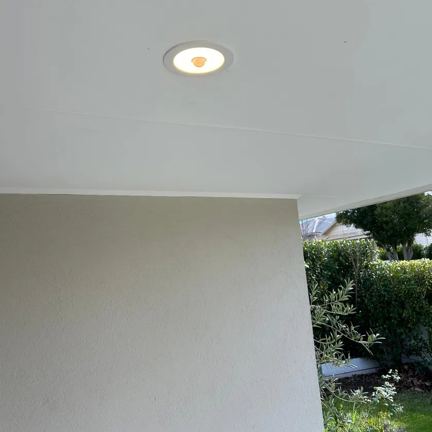 Recessed white LED downlight with built-in sensor in a clean painted ceiling under an outdoor covered area