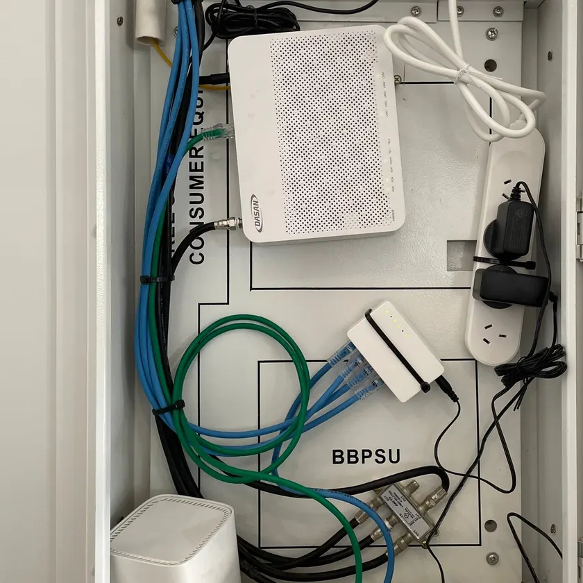 Open wall-mounted data cabinet with blue and green network cables tied neatly, modem, switch and power board