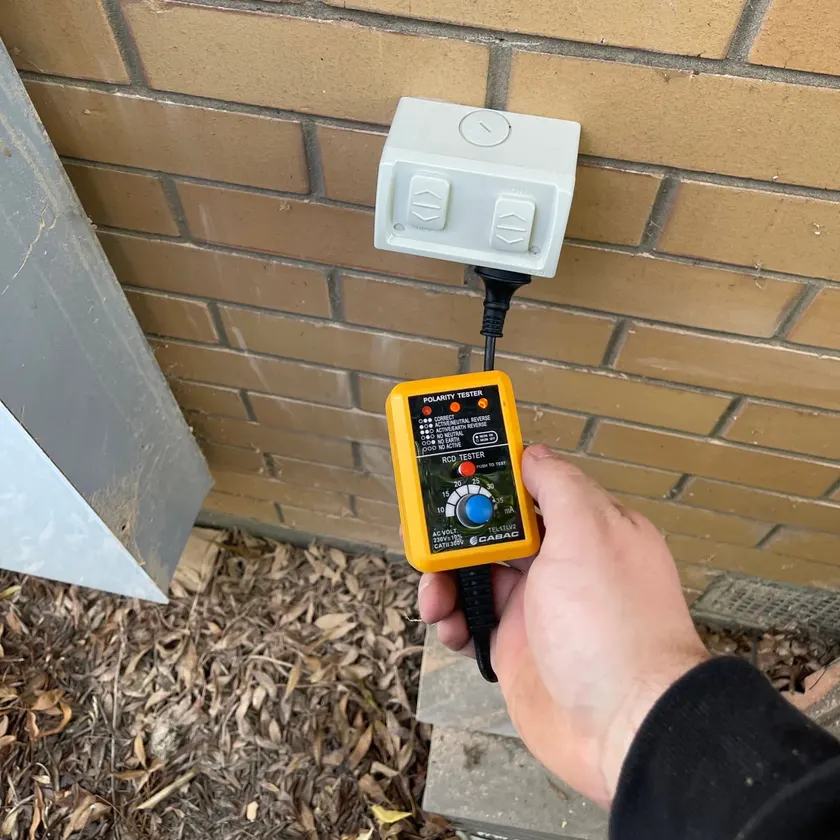 White weatherproof double power point on a brick wall being tested with a plug-in tester held by a tradie
