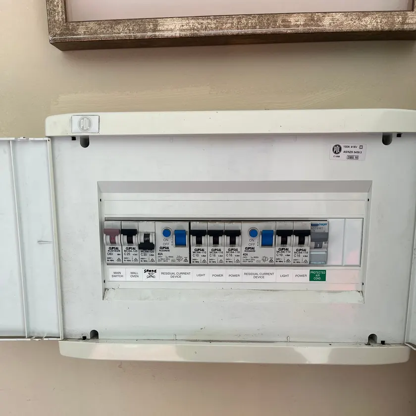 White flush-mount switchboard with Clipsal breakers, two safety switches and printed labels on a beige wall