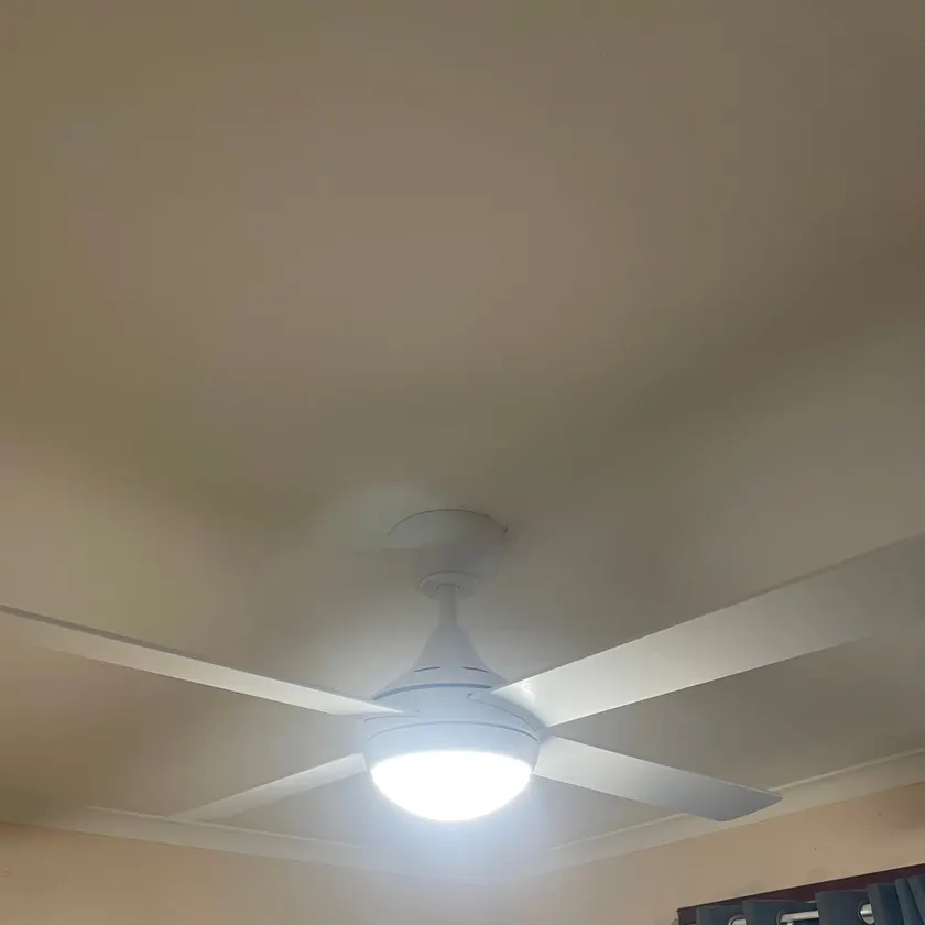White four-blade ceiling fan with light switched on, fitted in a bedroom corner