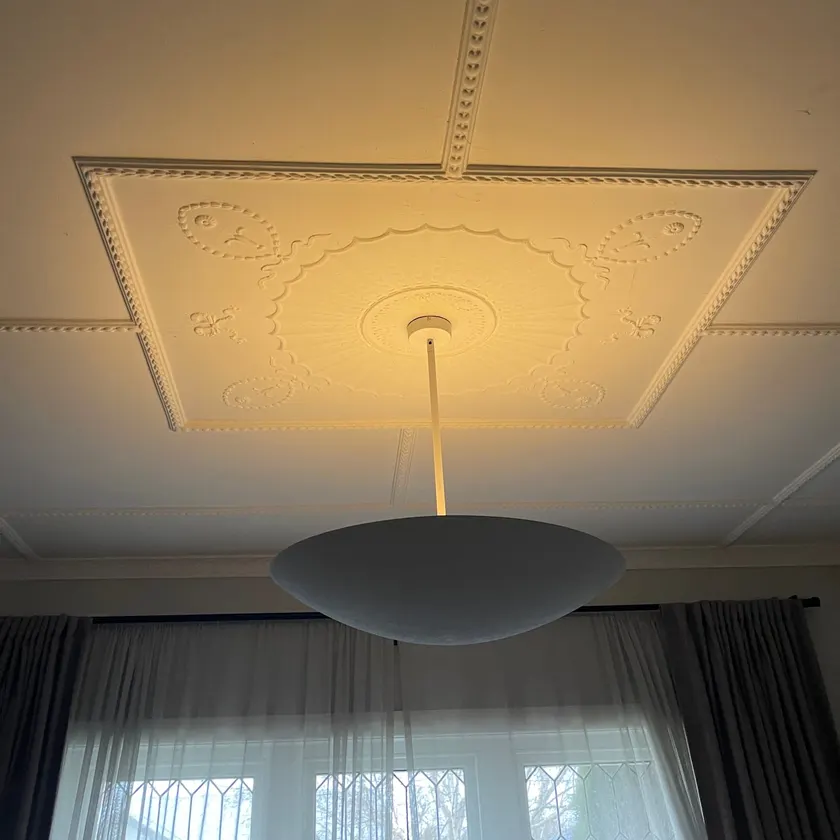 Modern white pendant light hanging from a decorative plaster ceiling rose in a period room with a curtained window