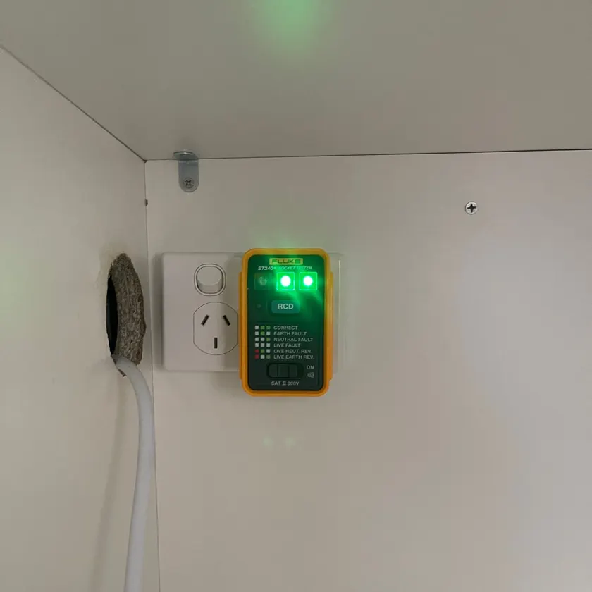 Socket tester showing green lights on a power point fitted inside a white cabinet with a neat white cable entering