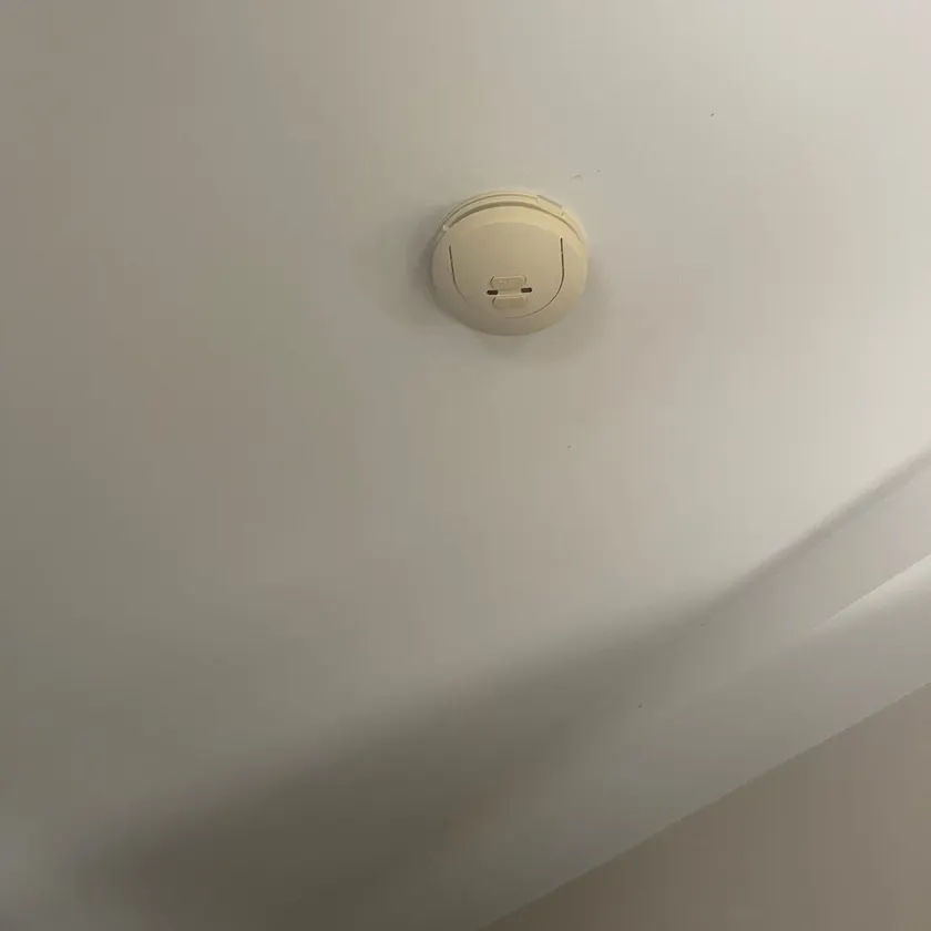 Cream smoke alarm fixed flat to a white painted ceiling