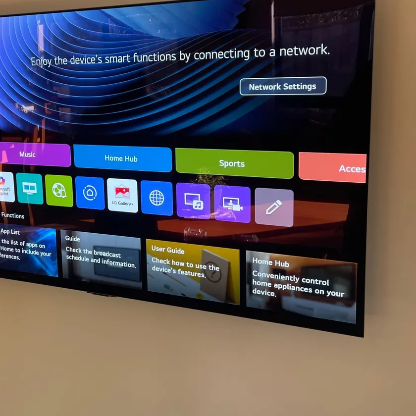 Flat-screen television mounted flat to a painted wall at an angle, showing a smart-TV menu screen