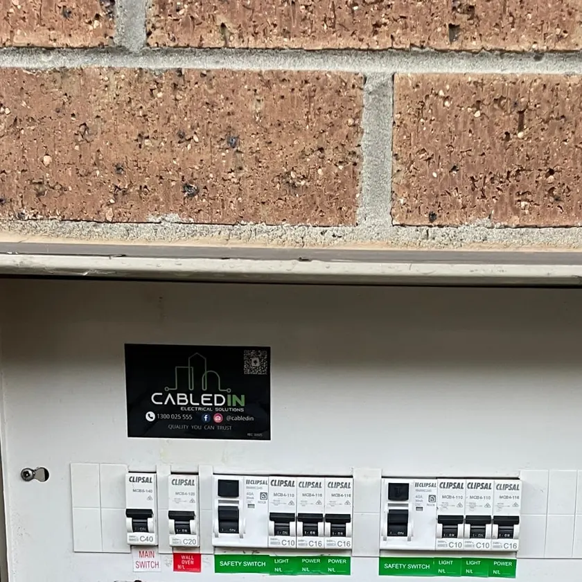 Outdoor meter box with a labelled Clipsal switchboard, two safety switches and a CabledIN sticker on a brick wall