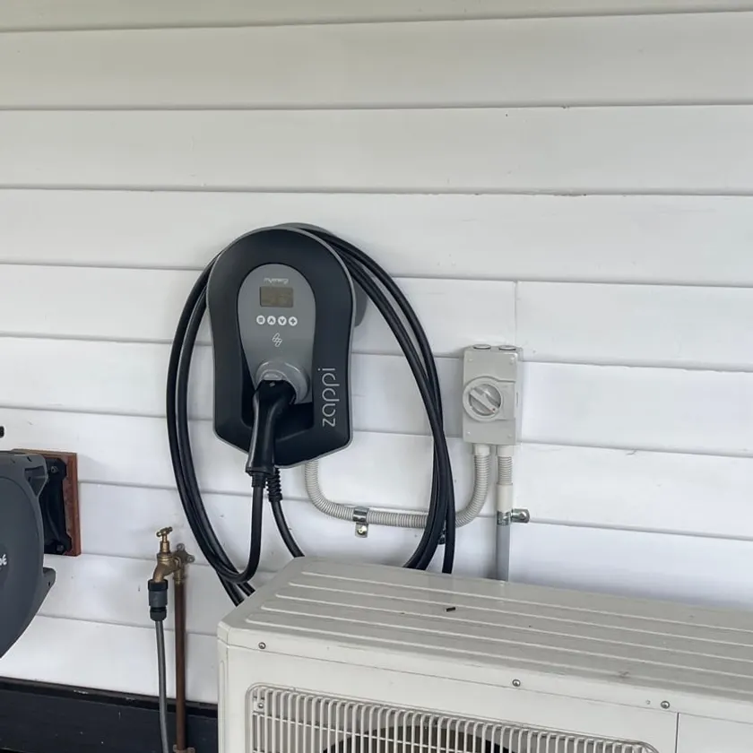 EV charger with its cable coiled and an isolator beside it on a weatherboard wall