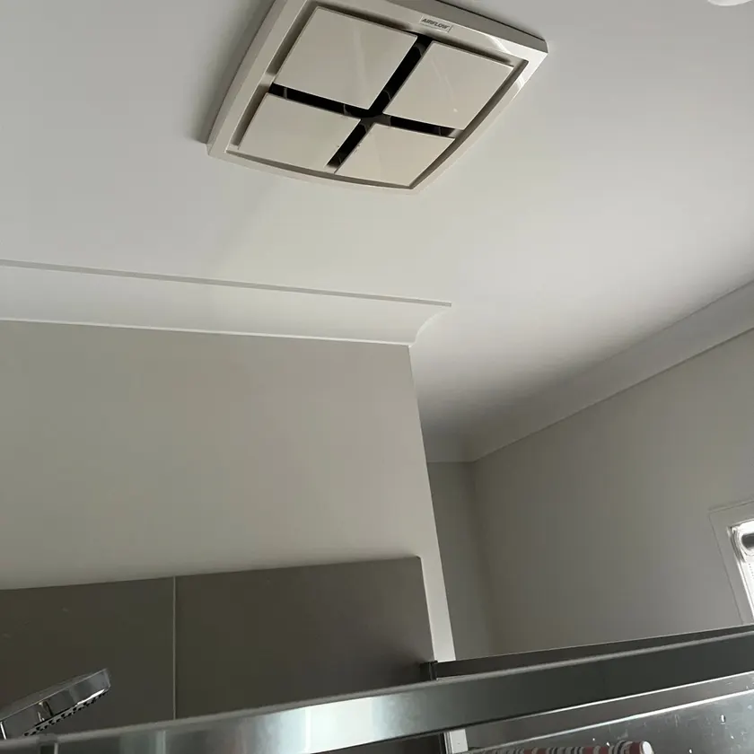 Square white exhaust fan fitted in a bathroom ceiling above a shower