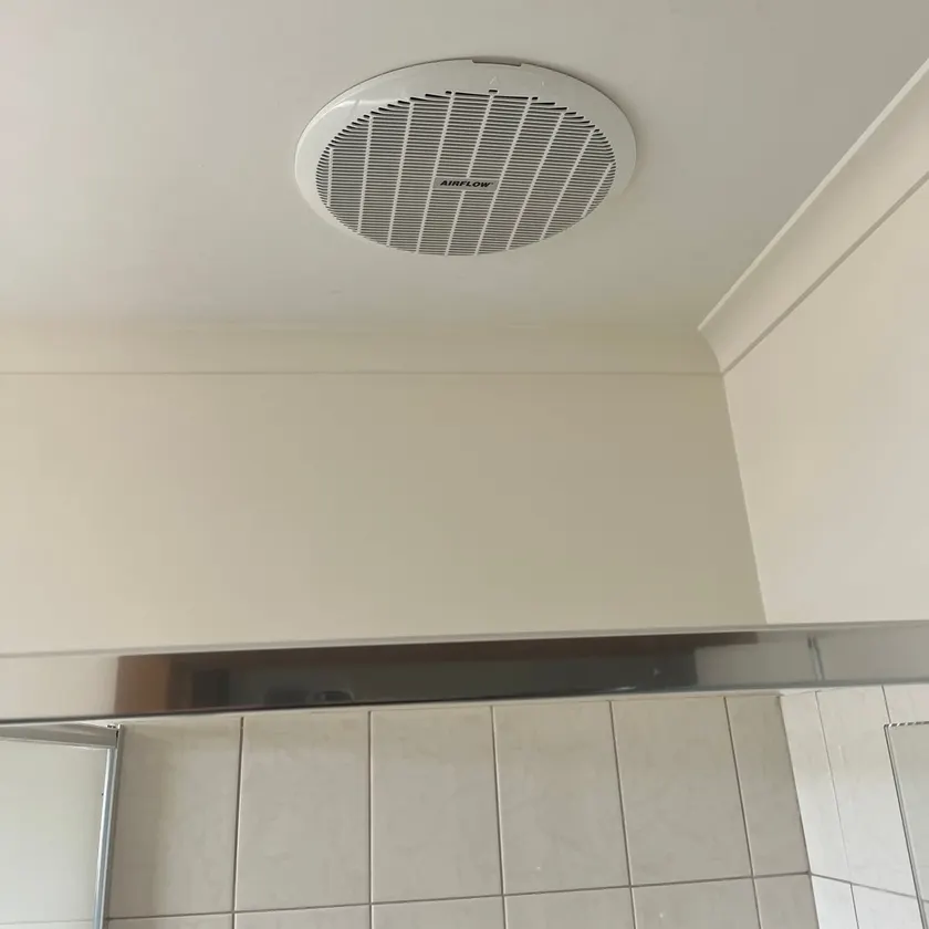 Round white exhaust fan grille fitted in a bathroom ceiling